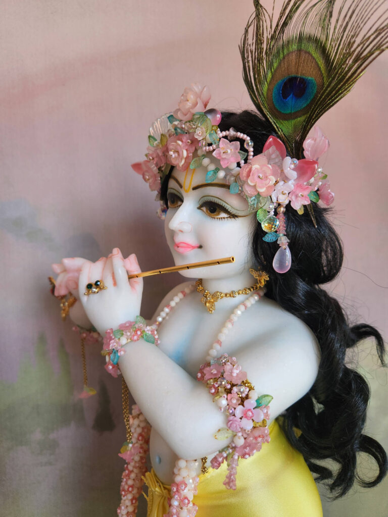 Krishna deity wearing flowery jewellery crown in pink