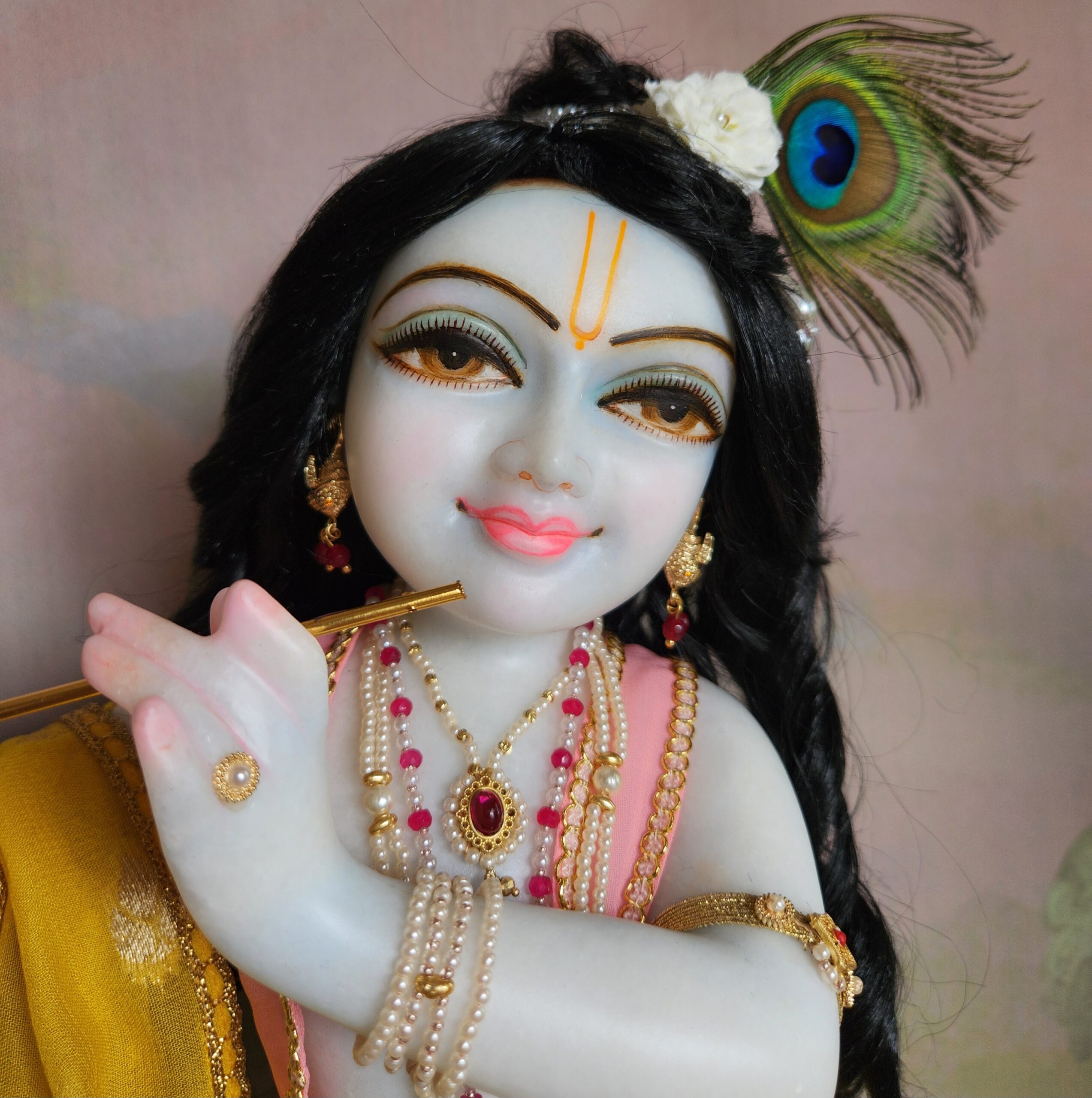 Close-up of the unique Krishna deity's hands. His delicate, pink-tipped fingers are playing lightly upon His golden flute, showcasing the intricate and loving detail of the hand-carved marble.