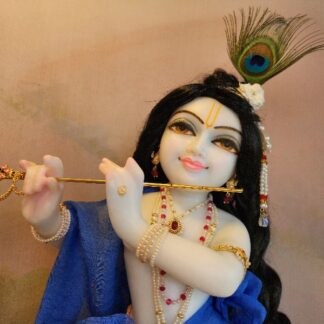 Close up view of upper torso of white marble unique carved krishna deity. Smiling face of deity and smiling eyes, wearing a black wig curling to his waist. dressed in blue and pearl jewellery and a peacock feather