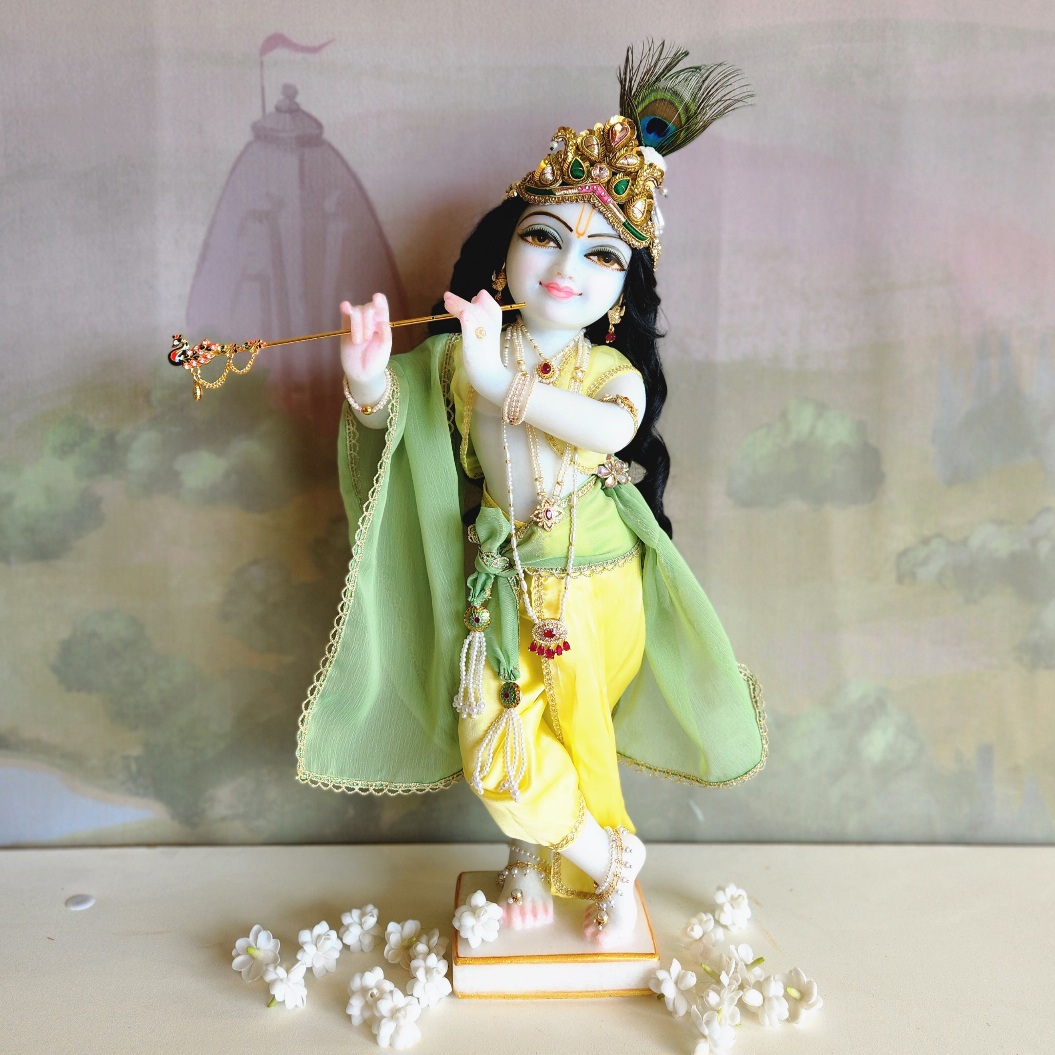 marble deity of krishna painted a soft delicate blue hue wearing delicate yellow and green soft dhoti