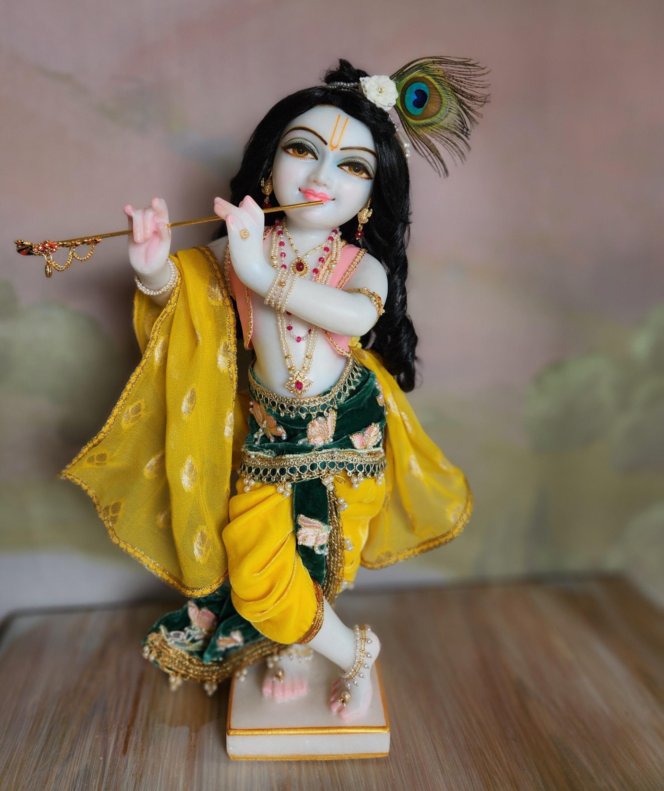 The unique Krishna deity dressed in one of His seven custom outfits: a yellow velvet silk dhoti with a green lotus-embroidered pleat and a matching pink vest. He is fully adorned with pearl and gold jewelry.