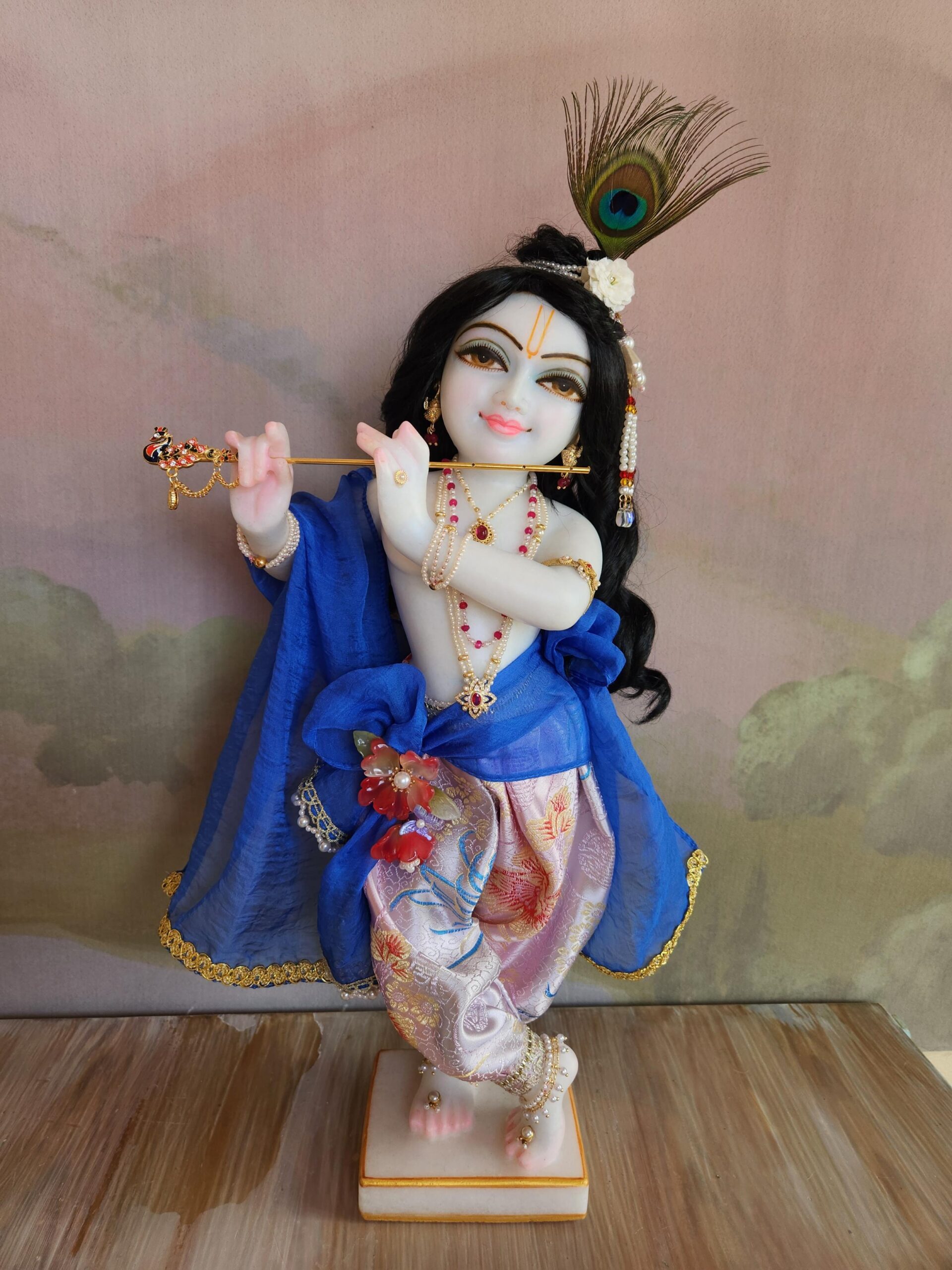 Close up view of upper torso of white marble unique carved krishna deity. Smiling face of deity and smiling eyes, wearing a black wig curling to his waist. dressed in blue and pearl jewellery and a peacock feather