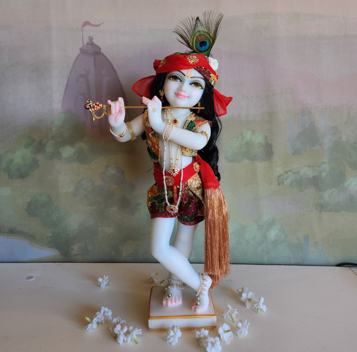 marble deity of krishna painted a soft delicate blue hue wearing autumnal colors of gold and orange and red