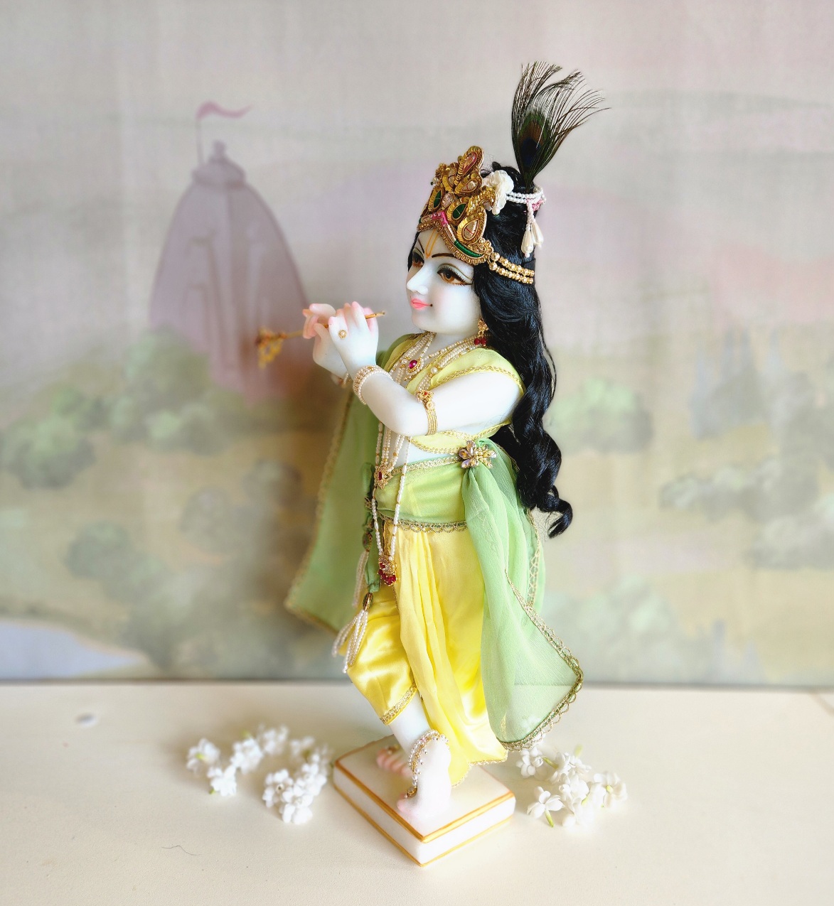 marble deity of krishna painted a soft delicate blue hue wearing yellow and green with crown and pearl jewellery