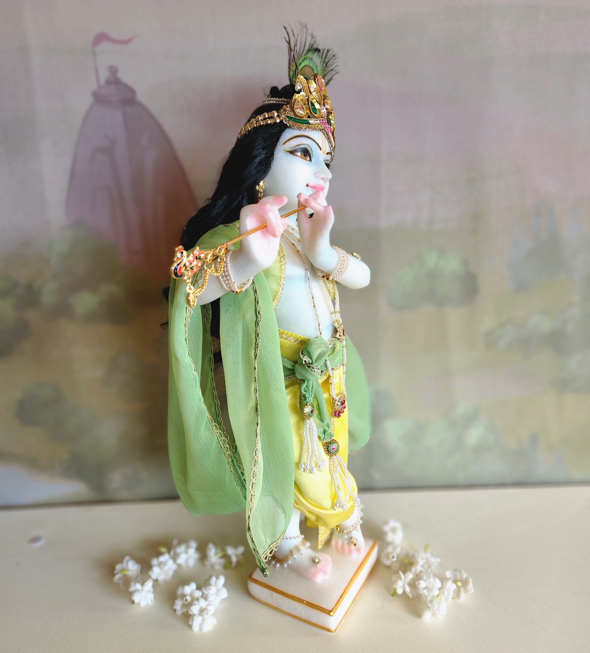 marble deity of krishna painted a soft delicate blue hue wearing flower garlands and pearl jewellery