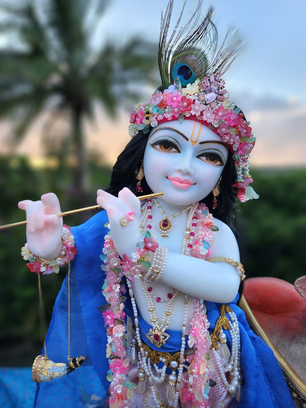 marble deity of krishna painted a soft delicate blue hue wearing flower garlands and pearl jewellery