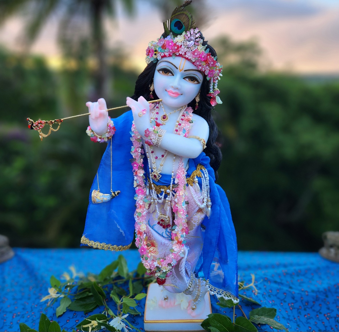 marble deity of krishna painted a soft delicate blue hue wearing flower garlands and pearl jewellery