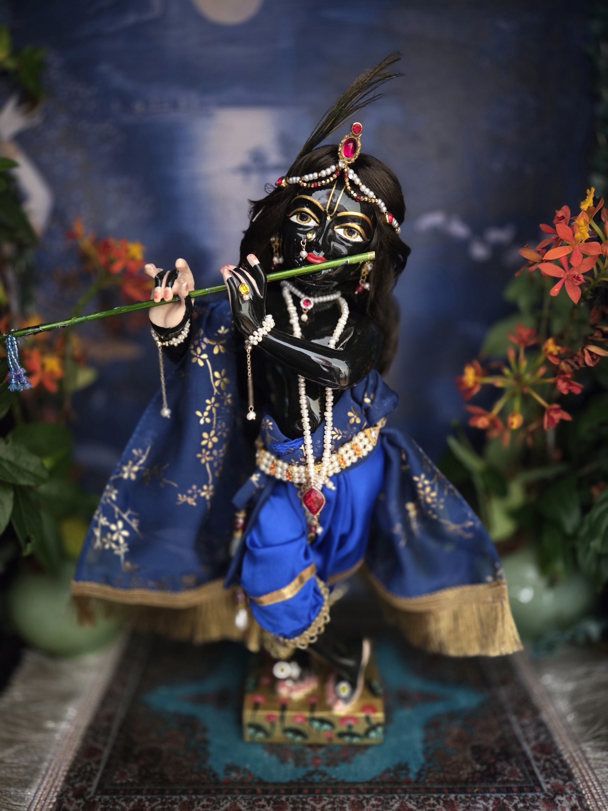 Gorgeous hand carved unique deity of Krishna in marble with a delicate hand painted finish, gentle storm cloud blue colorwash. delicate tilak markings and luminous eyes. Krishna deity, Chitta Chora, fully dressed playing flute pictured against a dark backdrop
