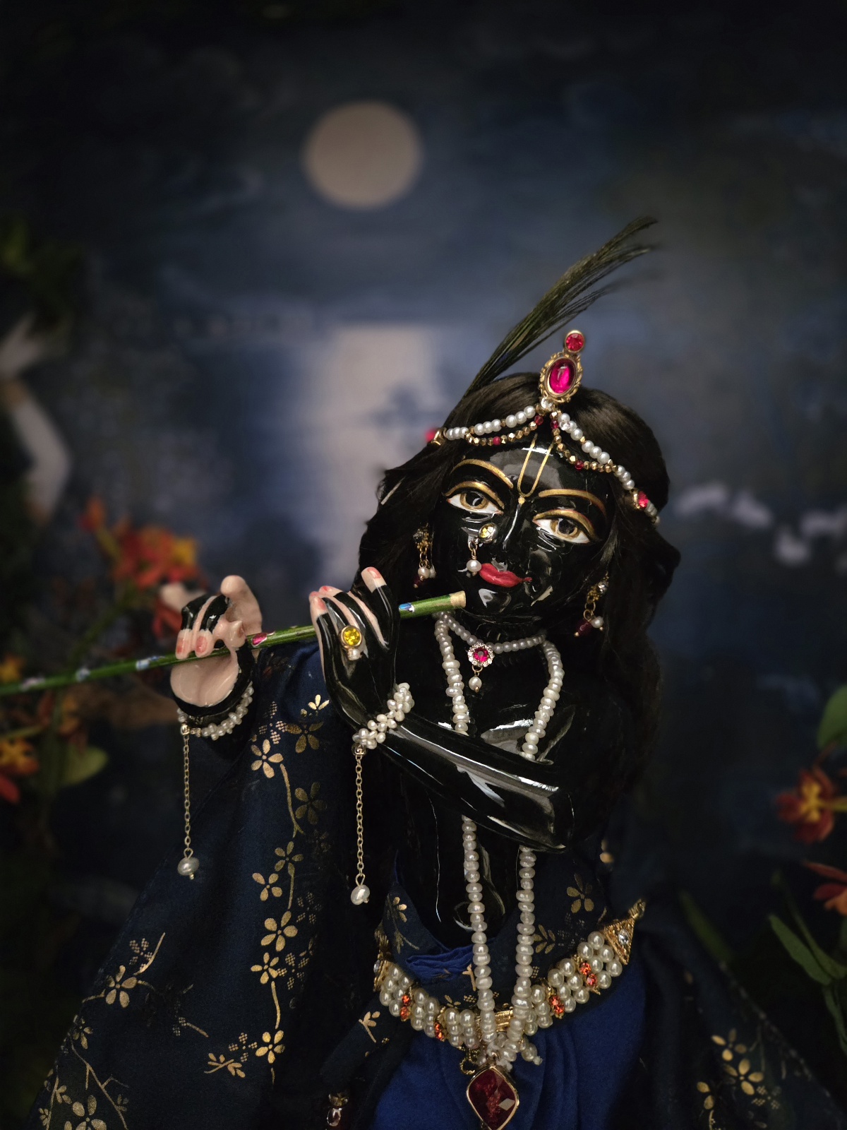 Gorgeous hand carved unique deity of Krishna in marble with a delicate hand painted finish, gentle storm cloud blue colorwash. delicate tilak markings and luminous eyes. Krishna deity, Chitta Chora, fully dressed playing flute pictured against a dark backdrop