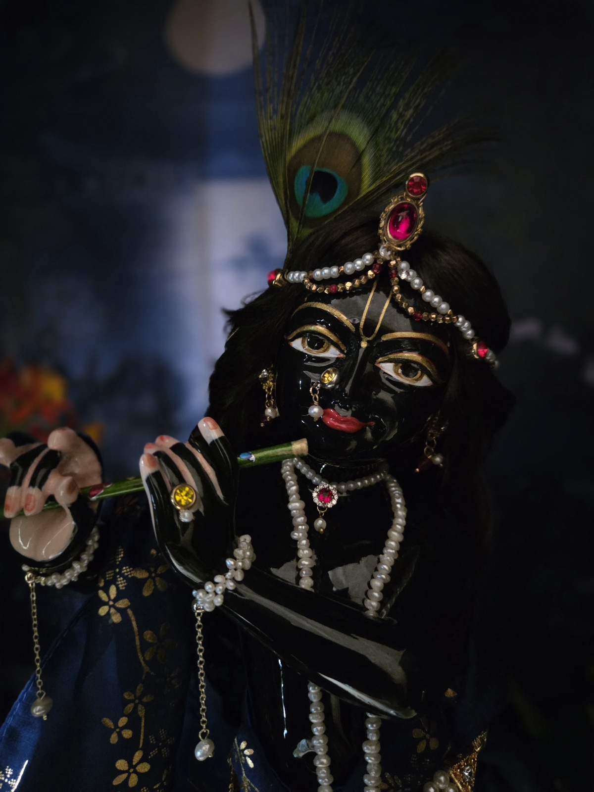 Gorgeous hand carved unique deity of Krishna in marble with a delicate hand painted finish, gentle storm cloud blue colorwash. delicate tilak markings and luminous eyes. Krishna deity, Chitta Chora, fully dressed playing flute pictured against a dark backdrop