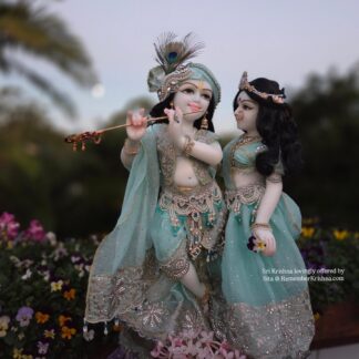 hari priya radha krishna deities in white marble photographed against a green forest wearing aqua shringar