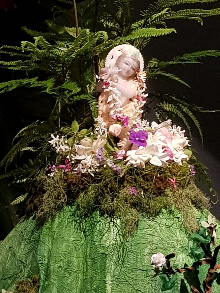close up look of marble deity of krishna on goverdhan hill covered with fresh foliage moss and tulsi