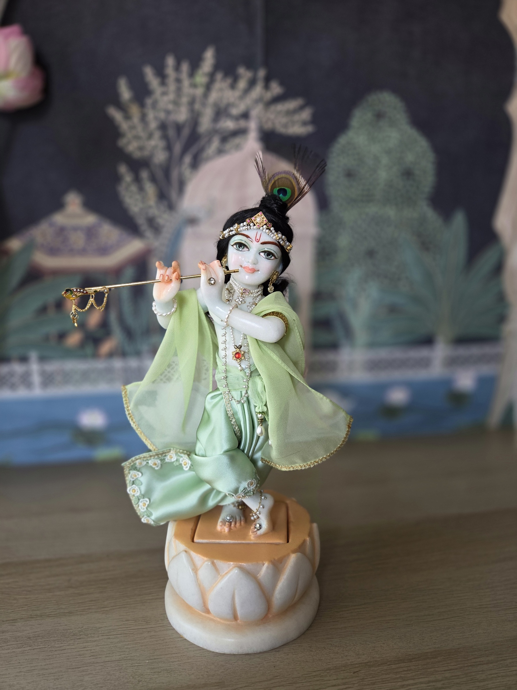 deity of Krishna named Balagopal carved in white marble with a mild blue colorwash. standing on a lotus carved base with miny shringar