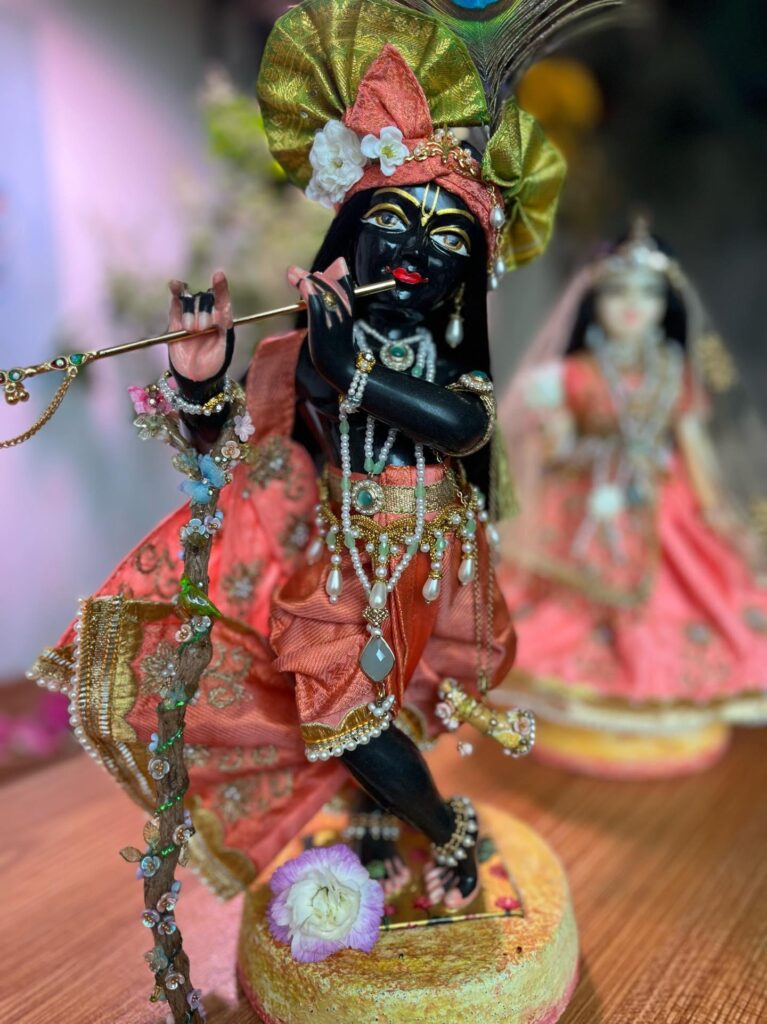 black marble deity of krishna dressed in peach shringar stands on special diy cement base with radha deity behind