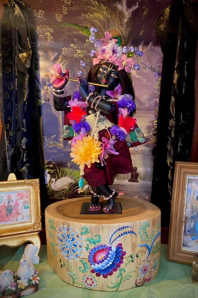 home deity beautiful black marble Krishna deity dressed in fresh flowers and standing on a specially carved wooden base